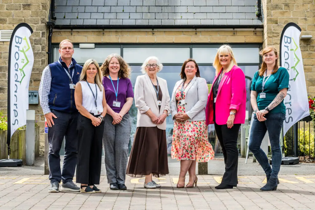 Broadacres staff stood in a line in front of a building with Broadacres flags either side.