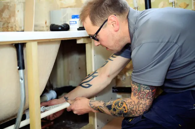 A plumber fixing an leak under a bath