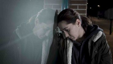 Sad depressed woman alone leaning on street window at night