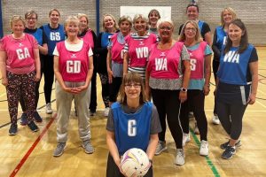 A group of 15 ladies wearing blue or pink netball bibs.