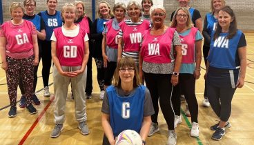 A group of 15 ladies wearing blue or pink netball bibs.