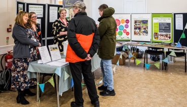 Two customers talk to colleagues from Broadacres at a stall in front of some posters.